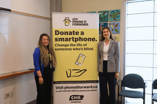A CNIB and Valet Wireless team member stand smiling beside a Phone It Forward banner.