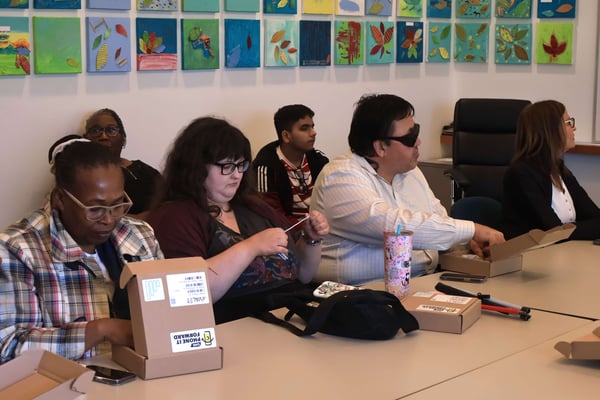Four participants reach into open smartphone boxes on a conference table.