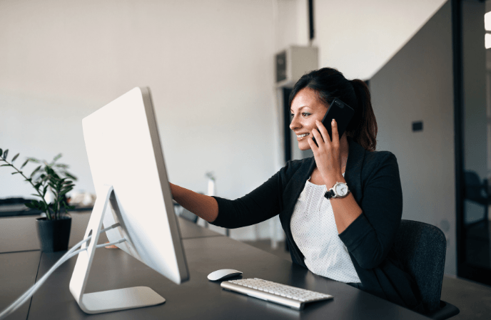 a woman with a phone looking at the pc